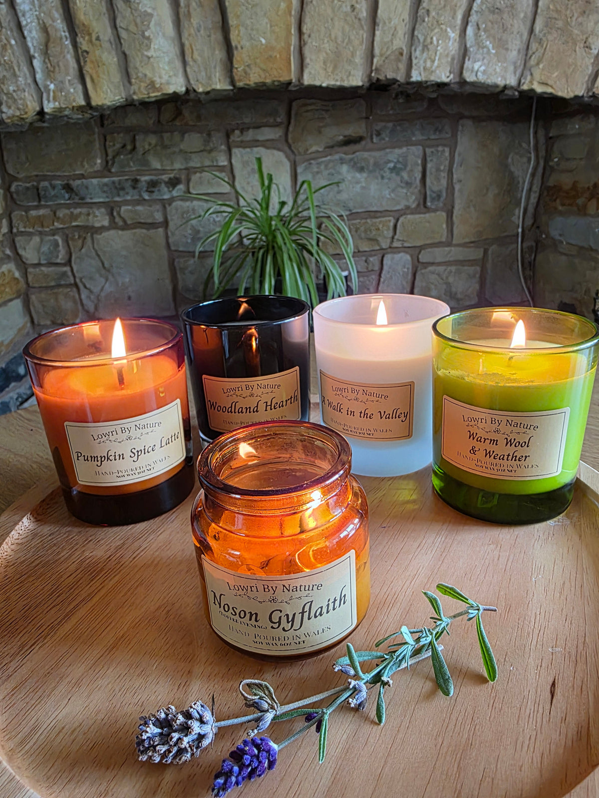 Lowri By Nature autumn soy wax candle collection burning on a wooden bowl with dried lavender, stone fireplace, Wales
